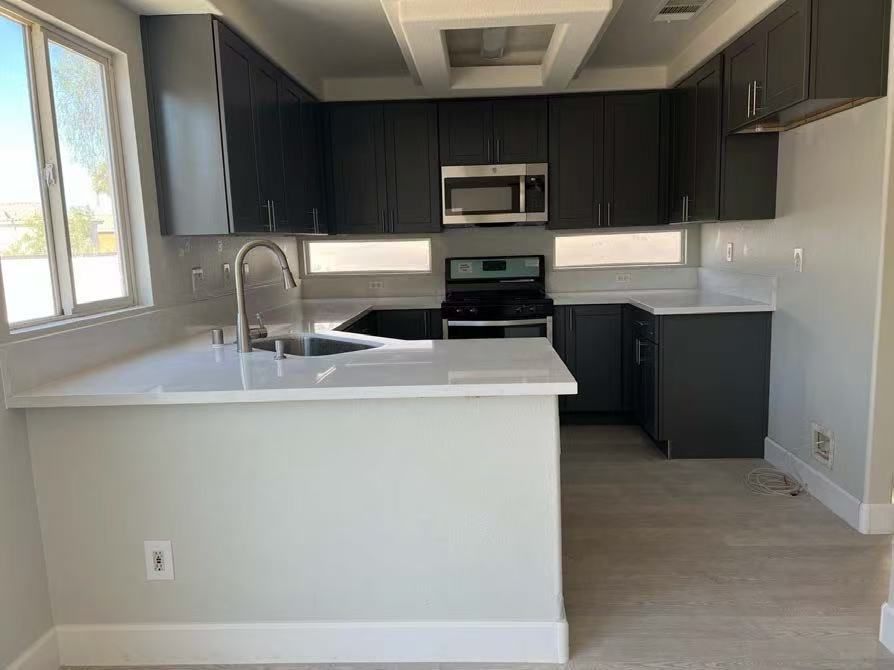 Modern kitchen with dark gray cabinets, white quartz countertops, stainless steel appliances, and a light-colored floor.