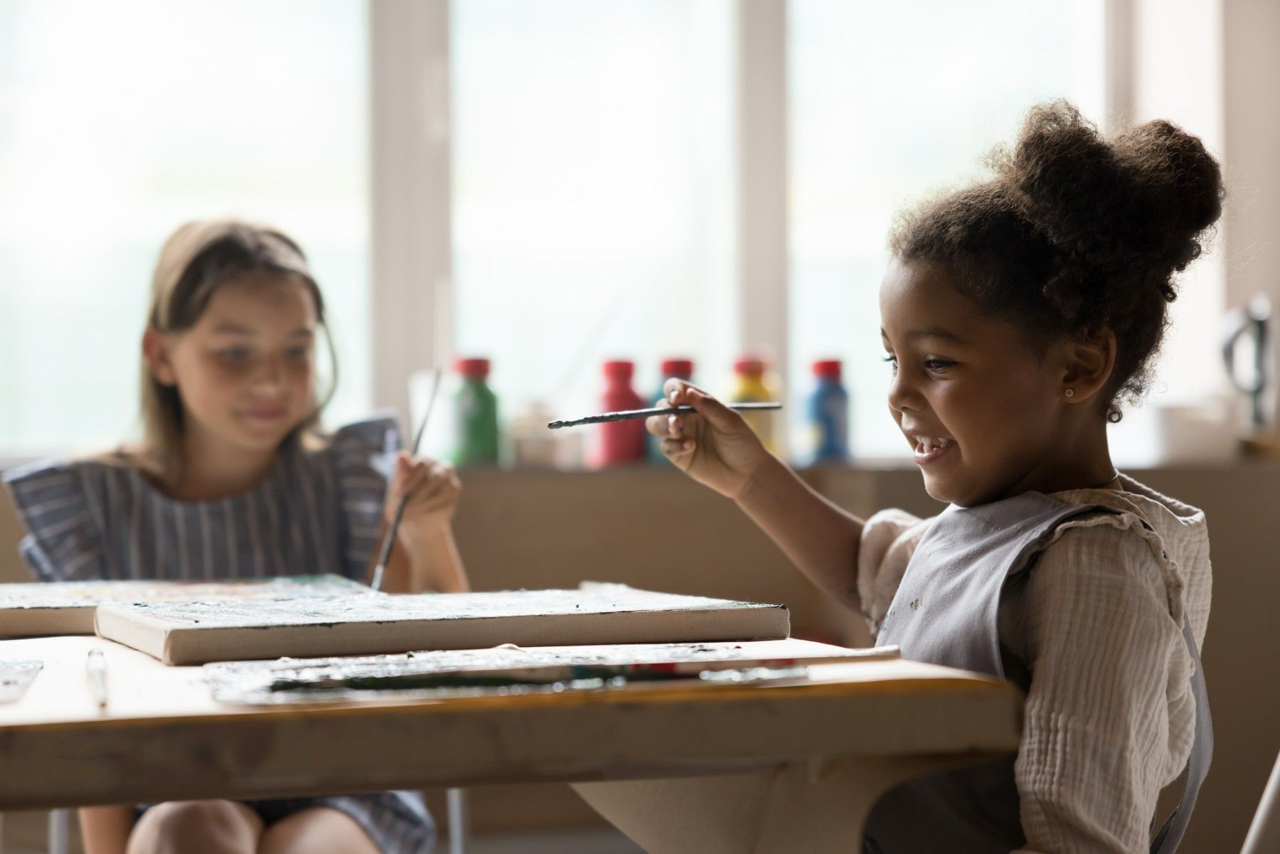 Two young girls are sitting at a table painting with watercolors.