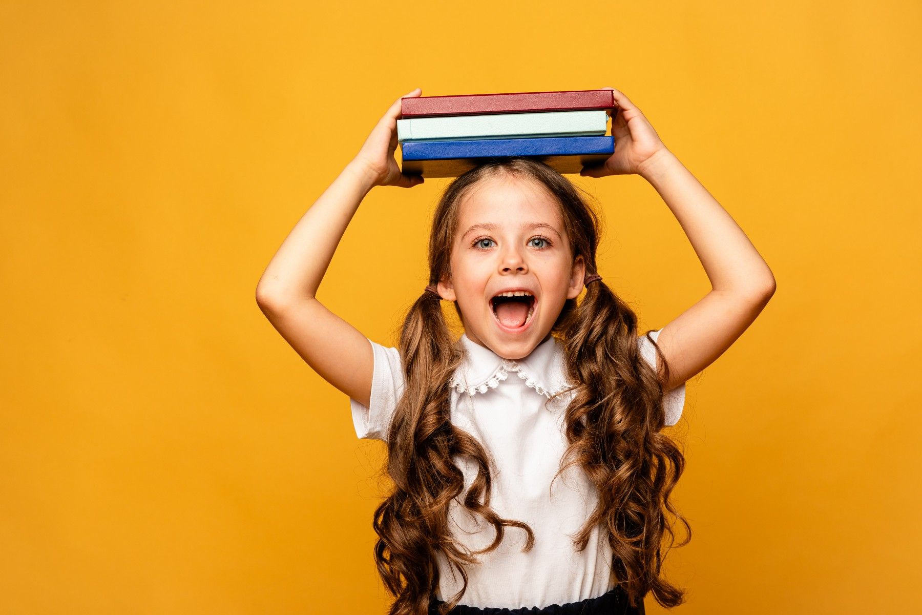 A little girl is holding a stack of books on her head.