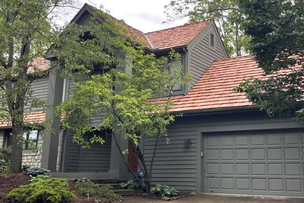 Two-story house with grey siding, terracotta roof, and attached garage; trees in front.