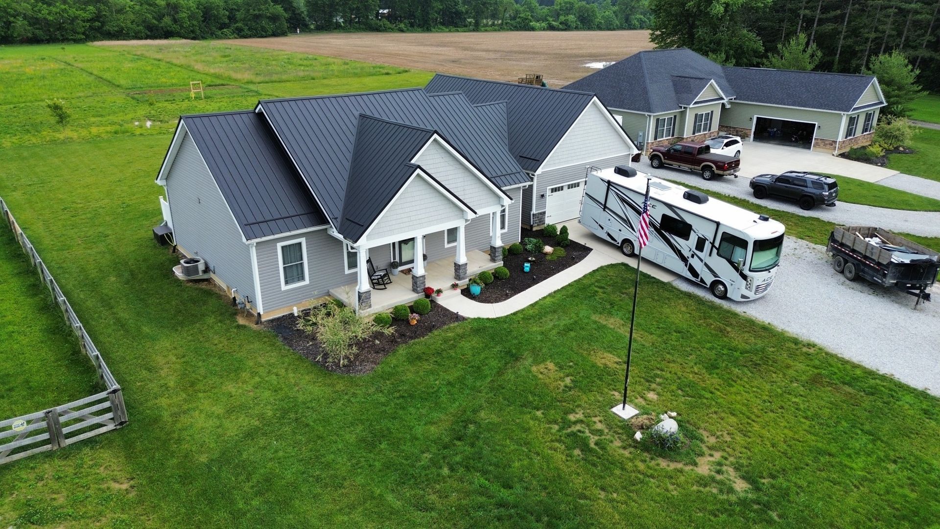 Gray house with black roof, RV parked in front, green lawn, blue sky.