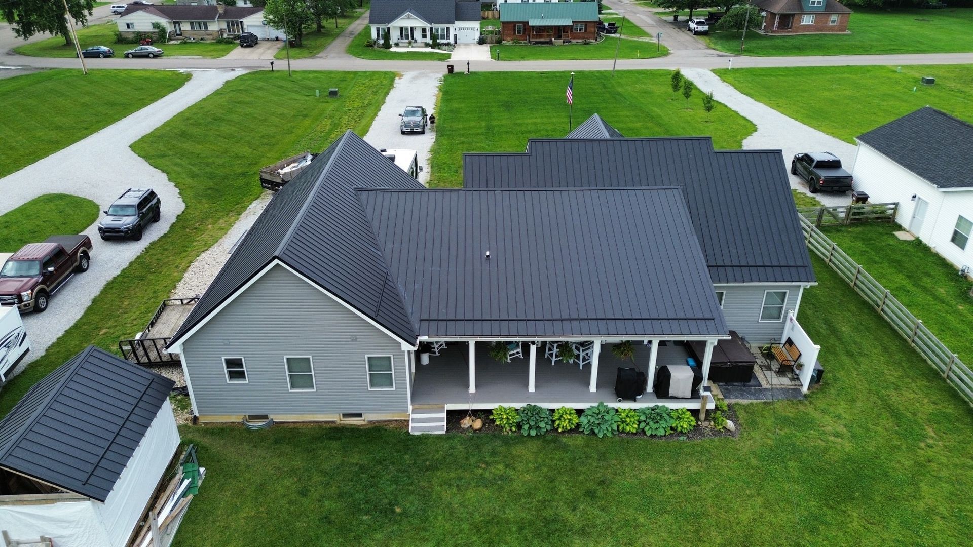 Aerial view of a gray house with a dark roof, surrounded by green grass, and other houses in a neighborhood.