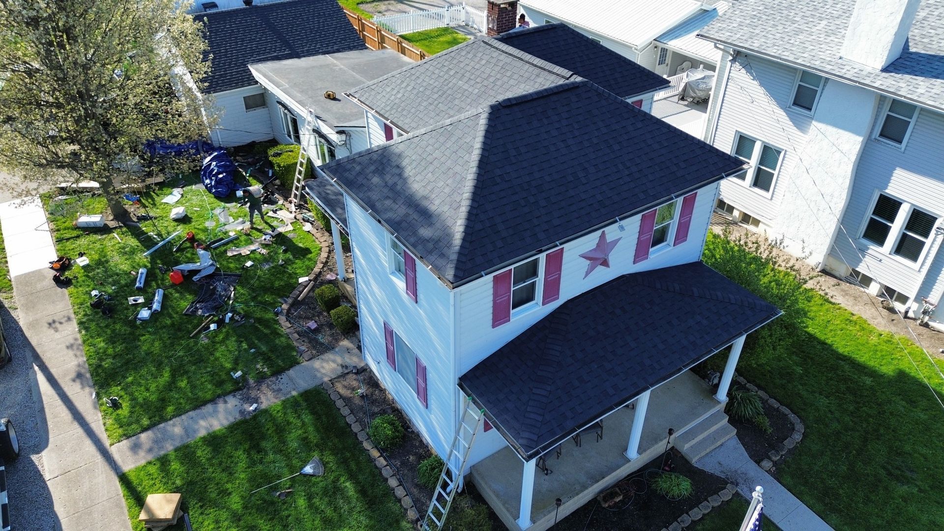 An aerial view of a two-story house with a dark gray roof and a red star on the front wall, grass lawn.