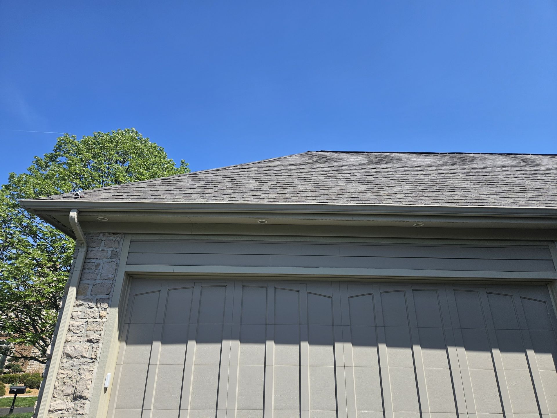 Garage with gray roof, light green siding, and clear blue sky.