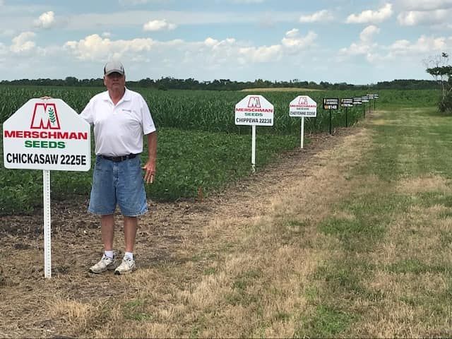 A man is standing in a field next to a sign that says merschman seeds.