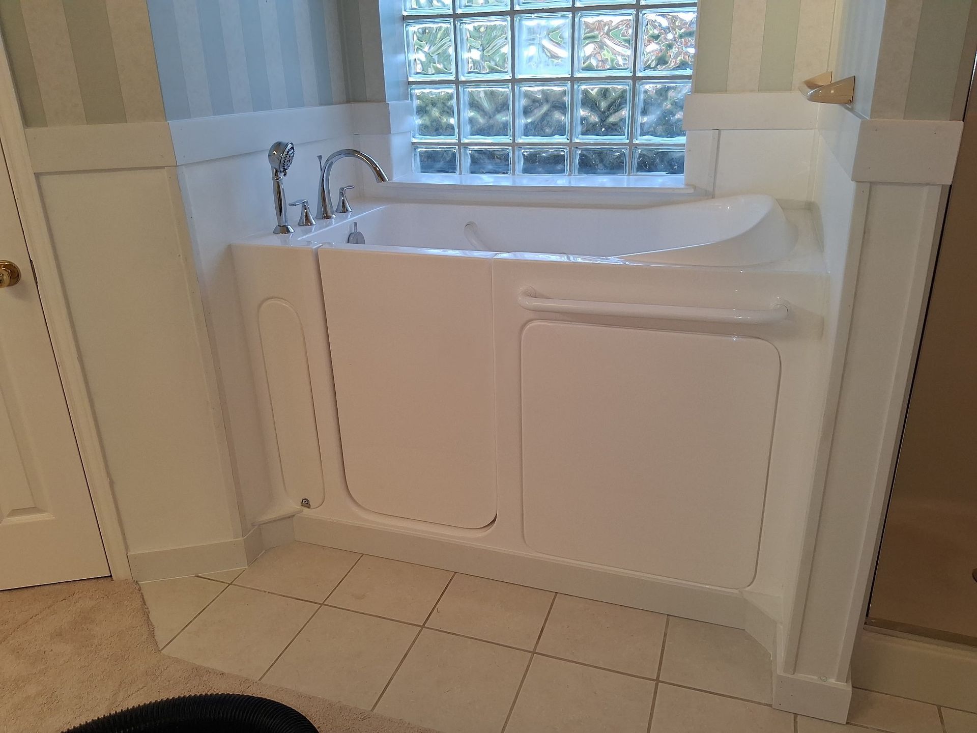 A walk in tub with a door in a bathroom next to a window.