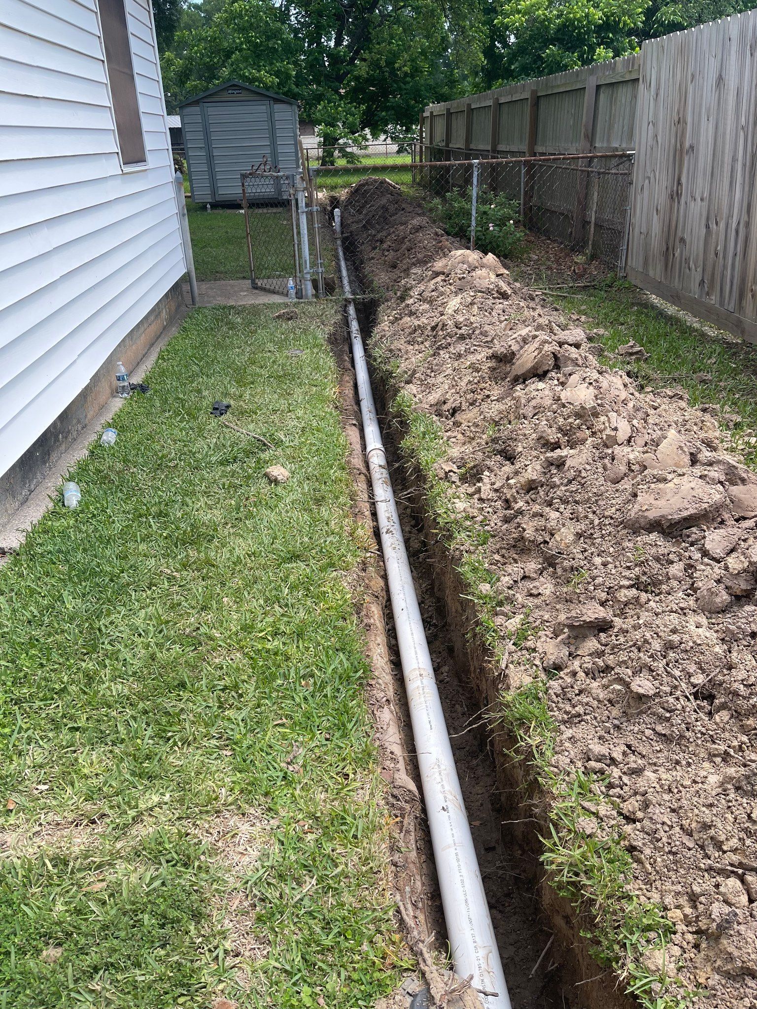 A drain pipe is being installed in the backyard of a house.