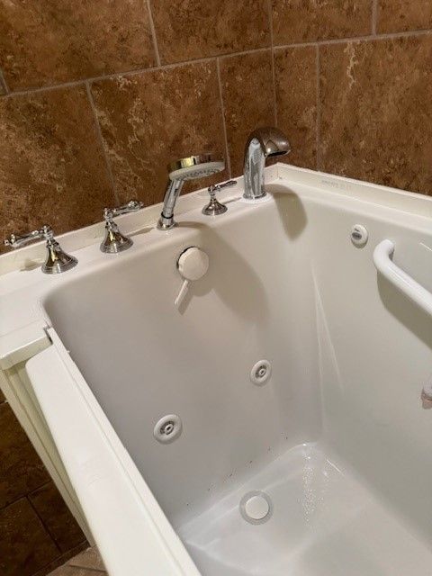 A white bathtub with a handle on the side is in a bathroom.