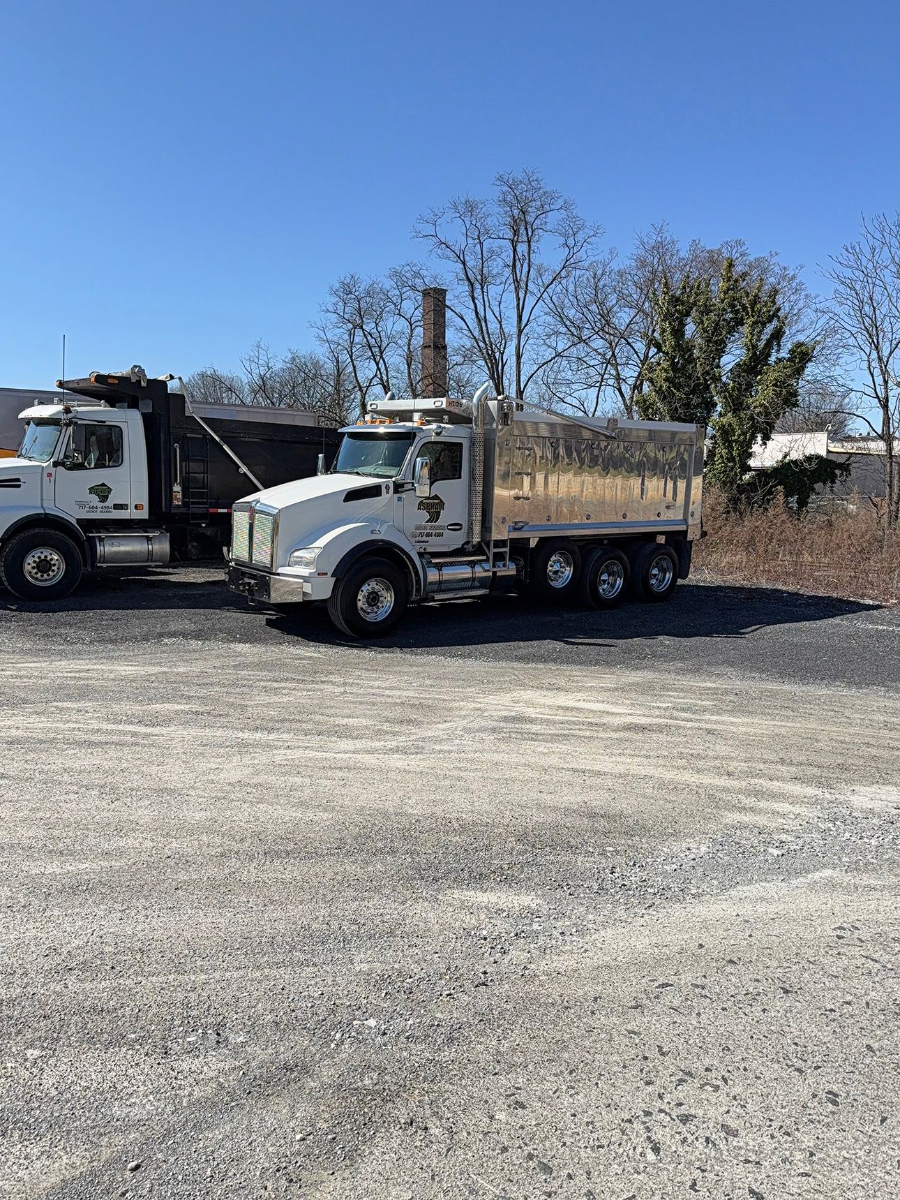 Two dump trucks are parked next to each other in a gravel lot.