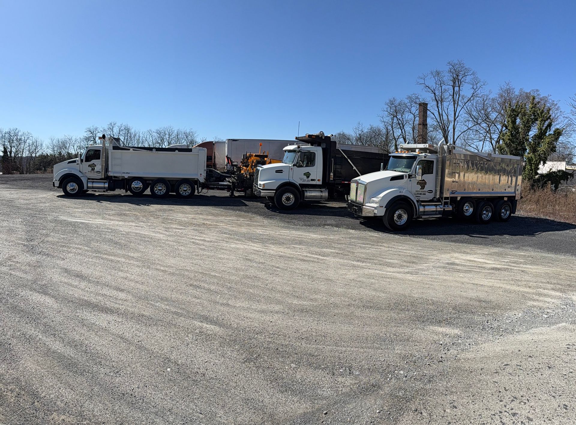 Three dump trucks are parked in a gravel lot.