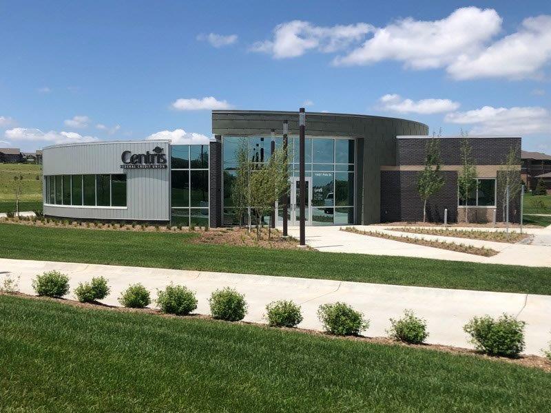 A large building with a lot of windows is surrounded by grass and bushes.