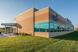 A large brick building with a lot of windows is sitting on top of a lush green field.