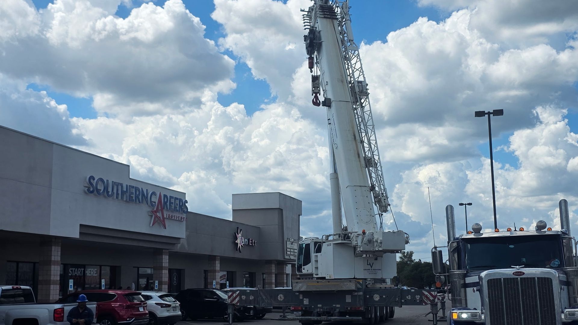 Large white crane truck outside a shopping center under a cloudy blue sky