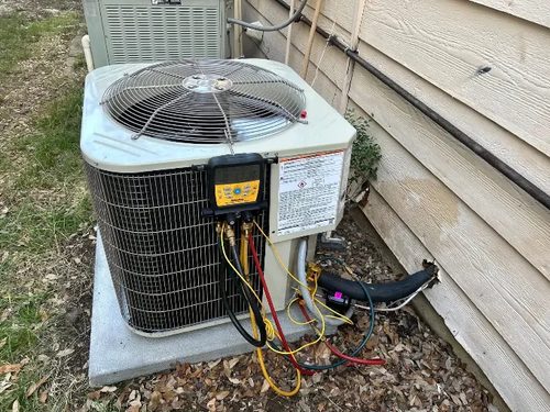 Outdoor HVAC condenser unit with exposed wiring beside a house wall.