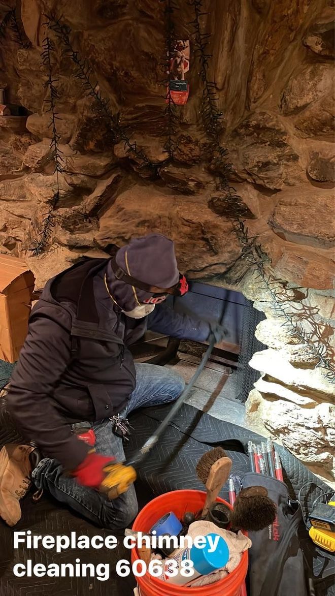 Man cleaning a fireplace chimney in a stone setting. He wears protective gear and uses tools.