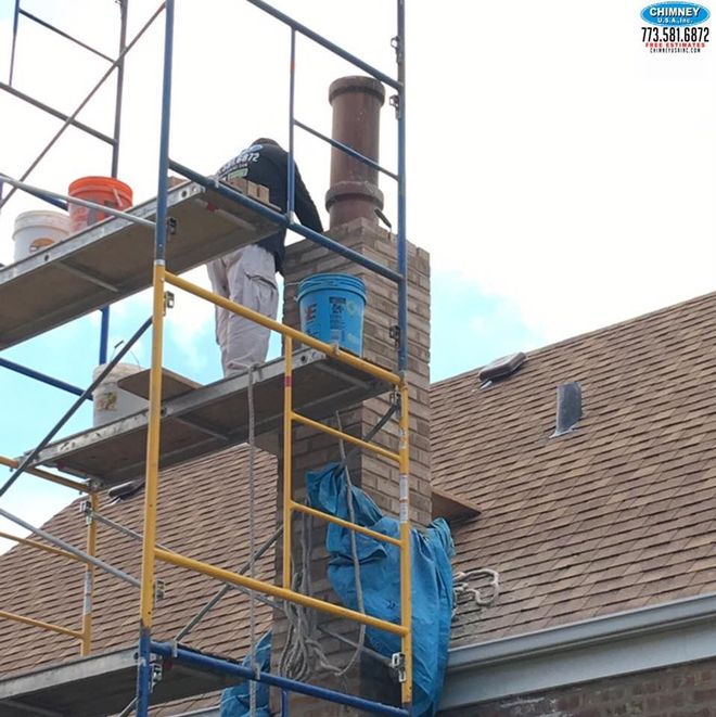Worker on scaffolding repairing a brick chimney on a house roof.