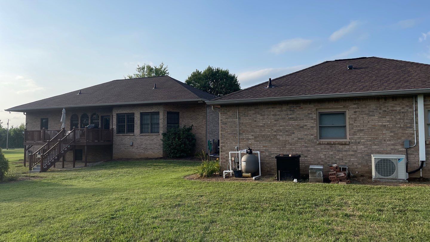 The back of a brick house with a large lawn in front of it.