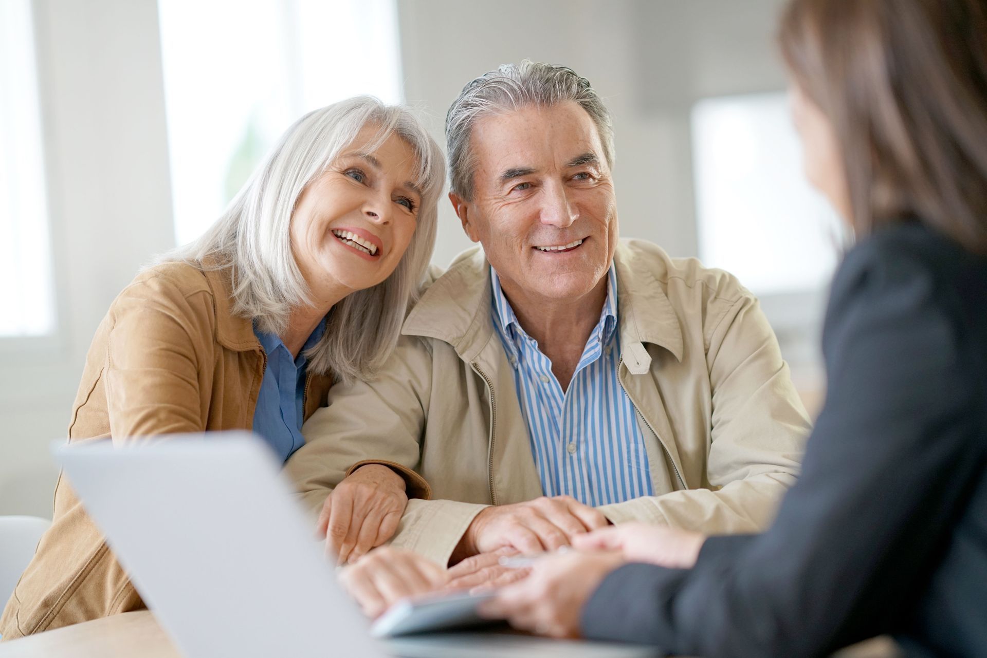 Smiling older couple at a table with a person using a laptop, possibly discussing finances.