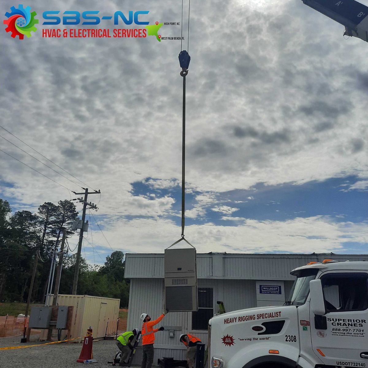 HVAC workers lifting a gray electrical cabinet with a crane outside a building under cloudy skies
