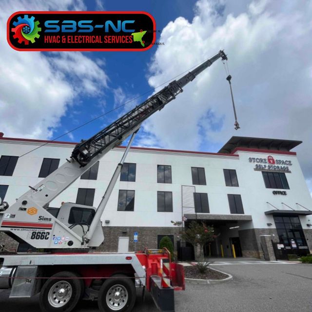 Bucket truck extended toward white building under blue sky, with SAS-NC sign and electrical service branding.