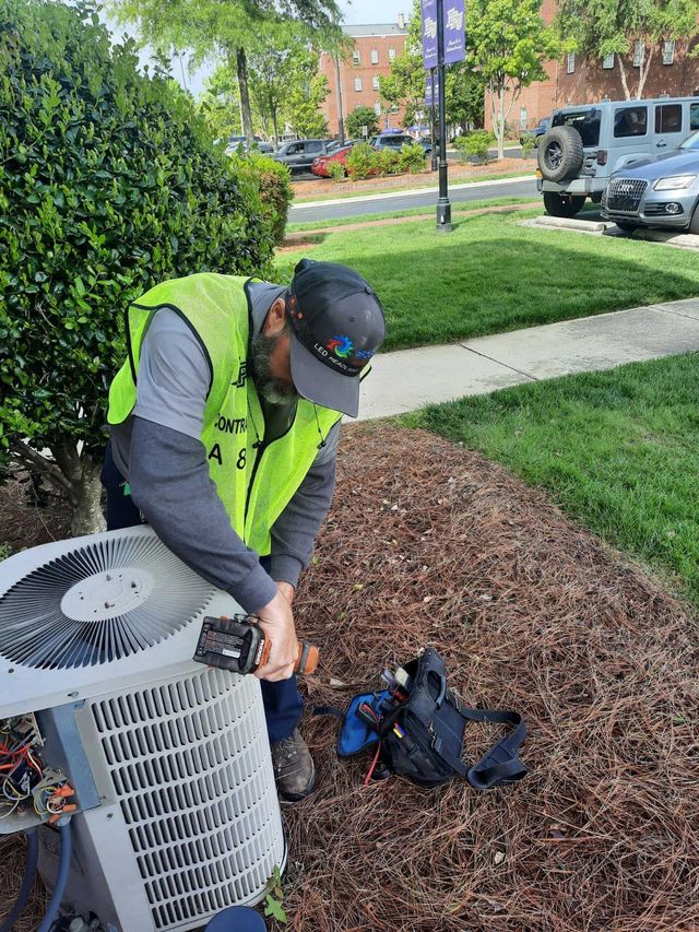 Worker in a neon vest repairing an outdoor air conditioner beside a sidewalk.