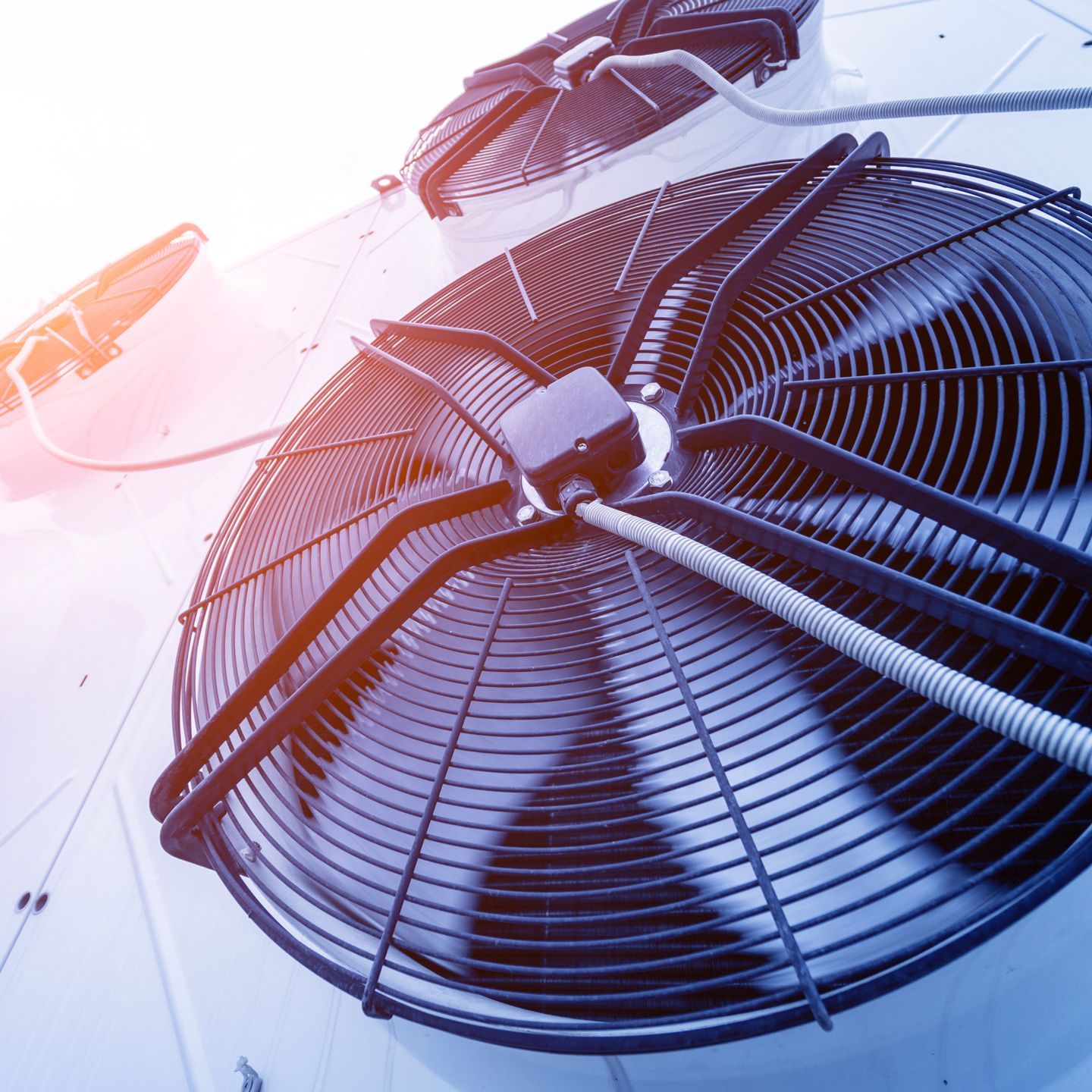 Large industrial cooling fan with metal blades, viewed from below against a bright sky