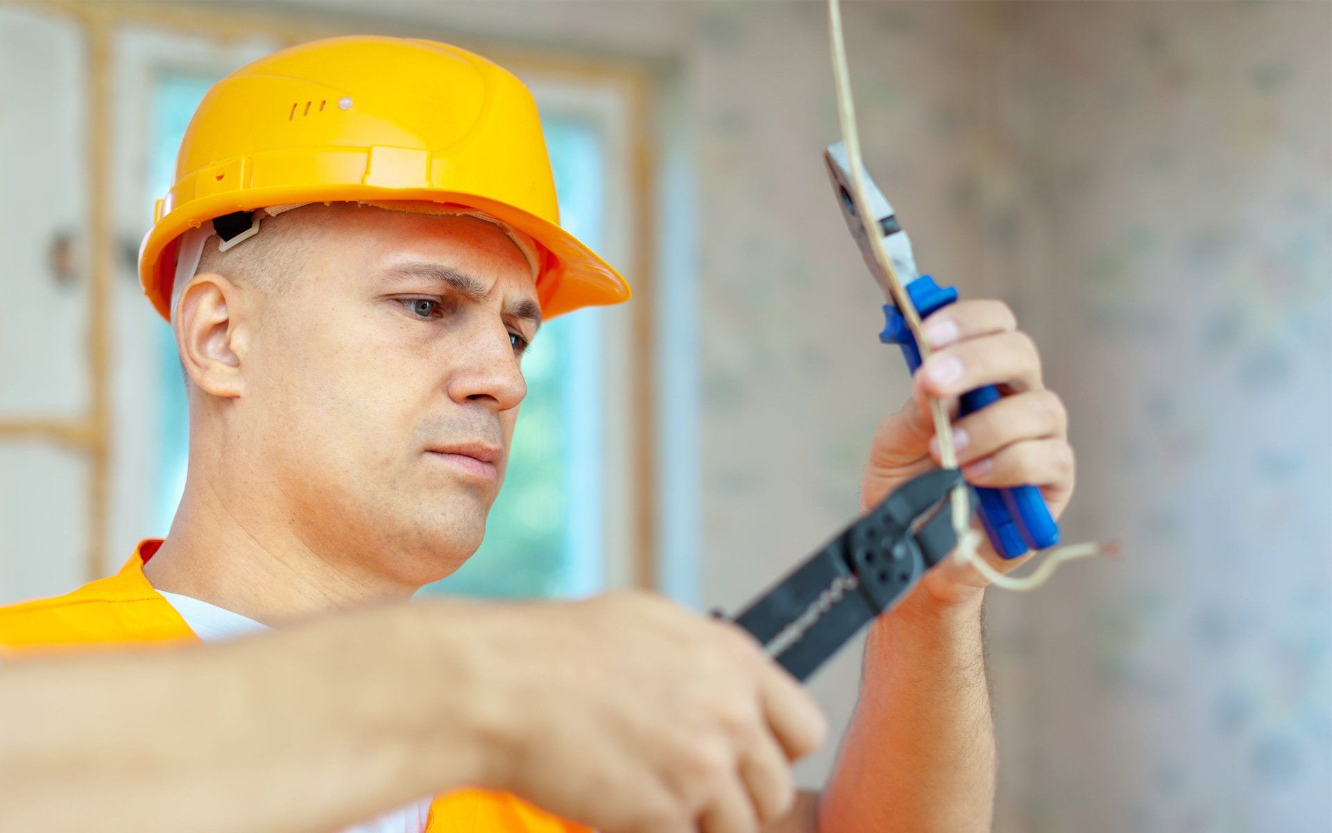A man in a hard hat is cutting a wire with a pair of pliers.