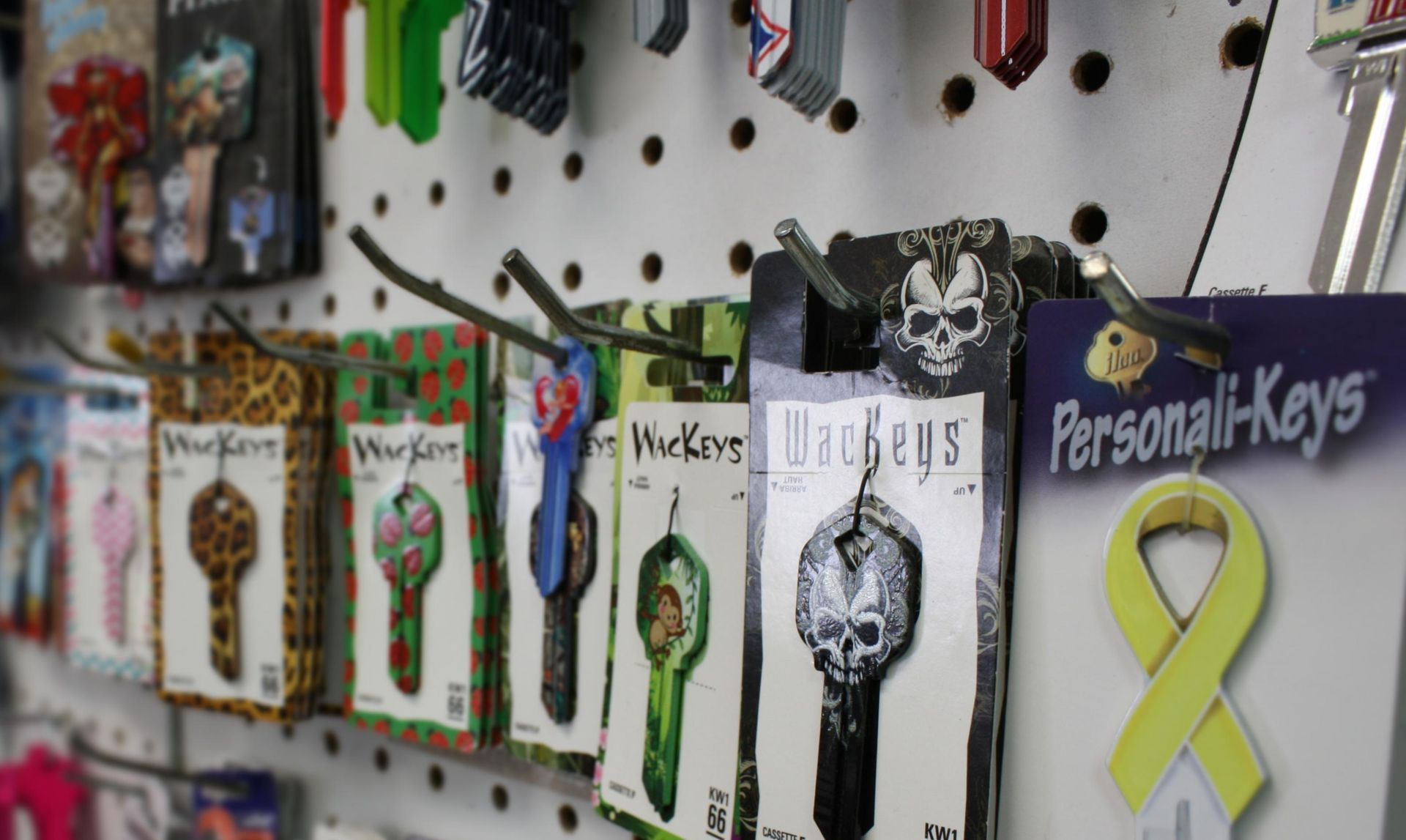 Keys hanging on a pegboard with decorative packaging; some are patterned with skulls and other designs.