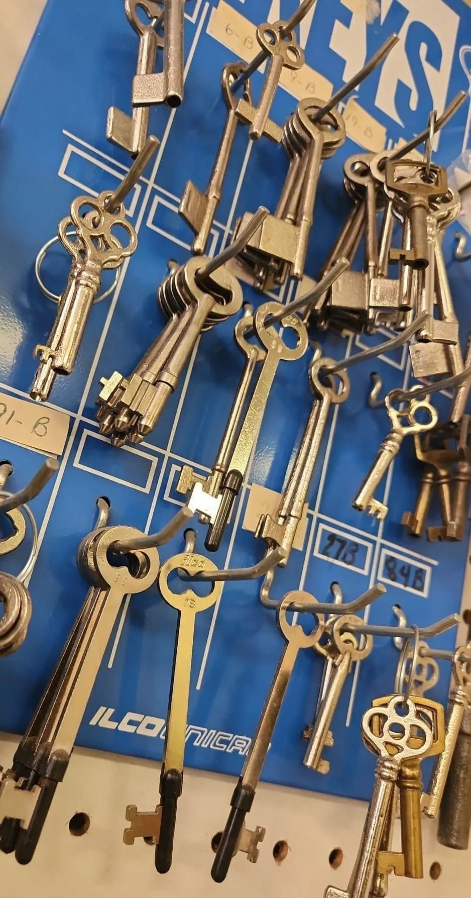 Keys hanging on a blue pegboard display, various shapes and sizes.