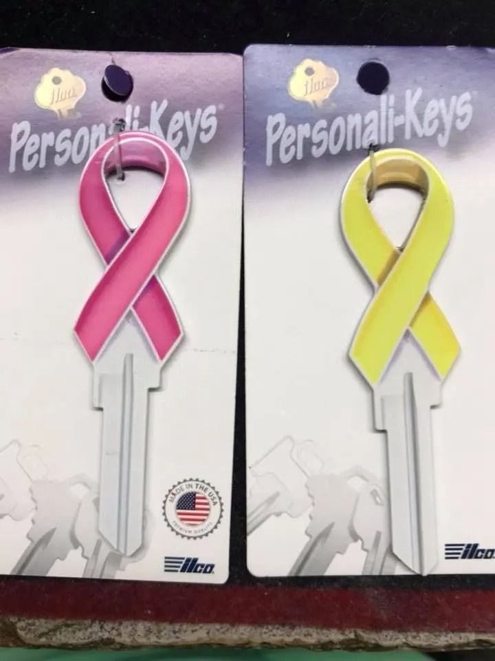 Two novelty keys shaped like ribbons: pink and yellow, on branded packaging.