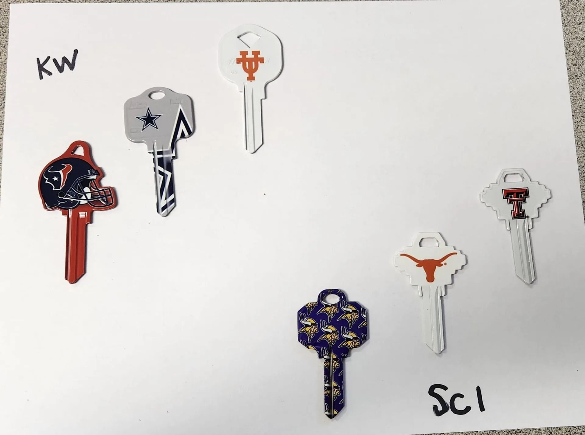 Keys decorated with sports team logos: Cowboys, Texans, Longhorns, Cougars, and others, on a white background.