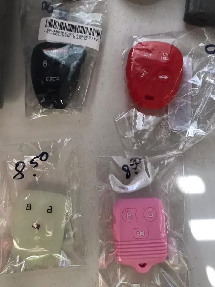 Four colored car key fobs in plastic bags: black, red, white, and pink, with prices listed