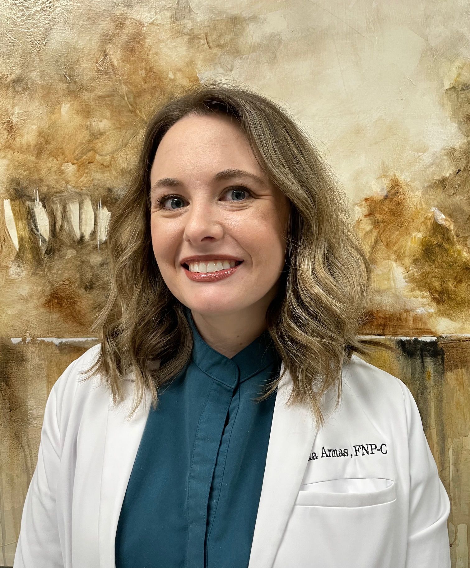 A woman in a white lab coat is smiling in front of a painting.