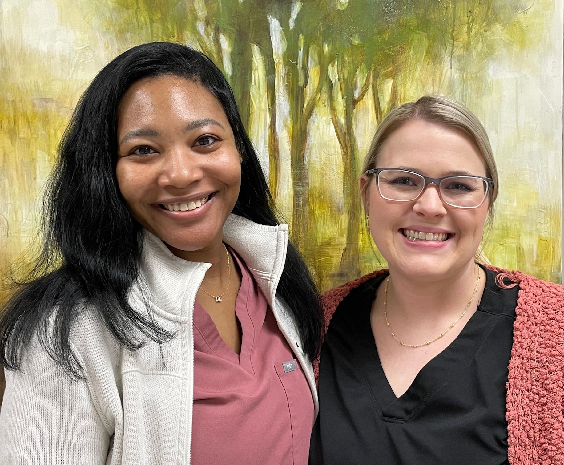 Two women are posing for a picture in front of a painting.