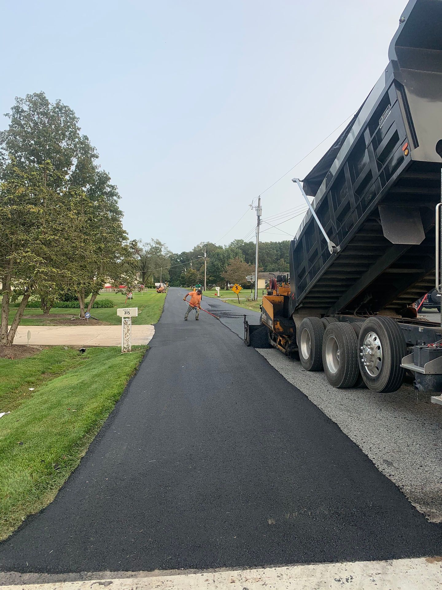 Fresh black asphalt being laid on a road beside a large dump truck, with workers in the distance