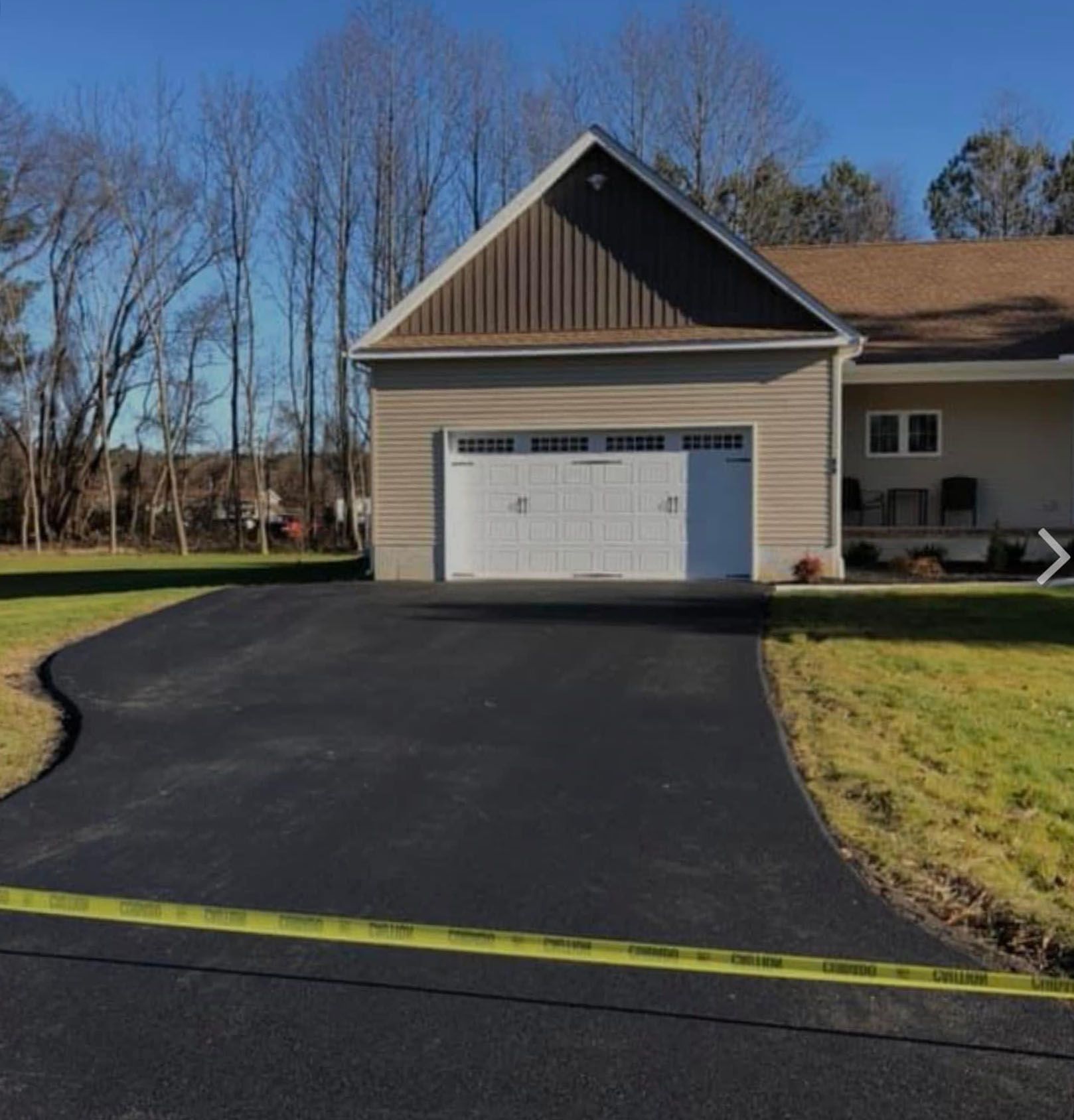 Fresh black asphalt driveway curving to a beige house with white garage door under a bright blue sky