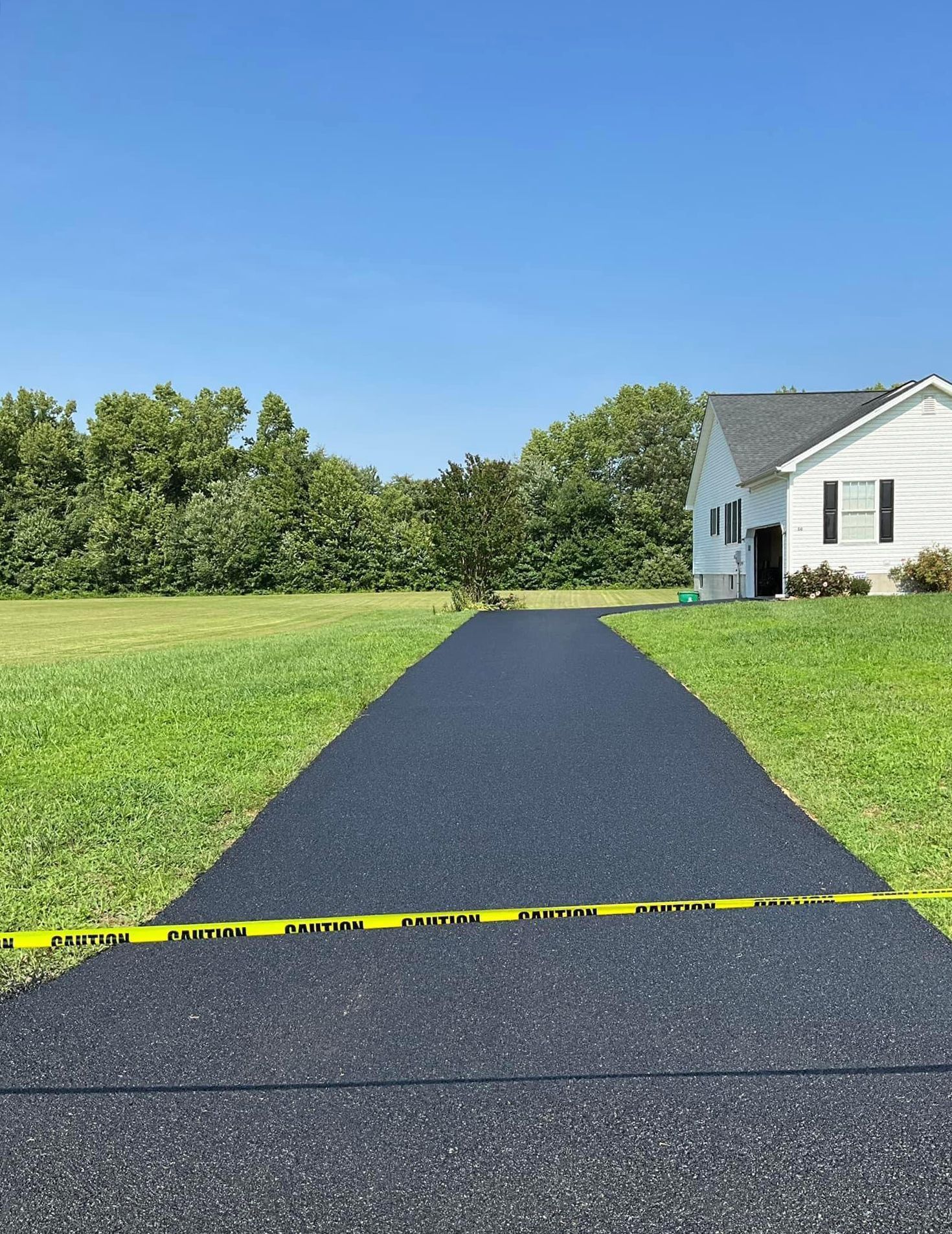Fresh black asphalt path leading to a white house across a green lawn, with yellow caution tape in front