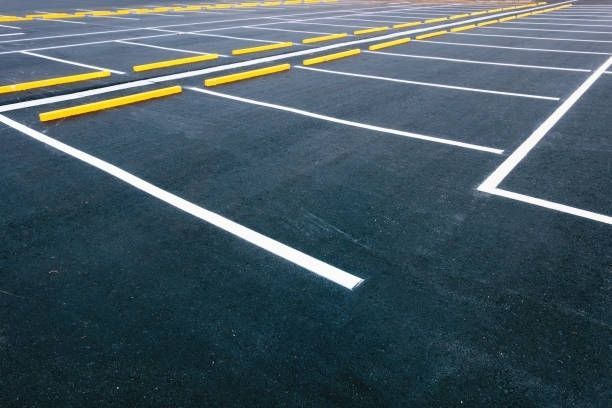 Empty parking lot with dark pavement and white lane markings under a cloudy sky