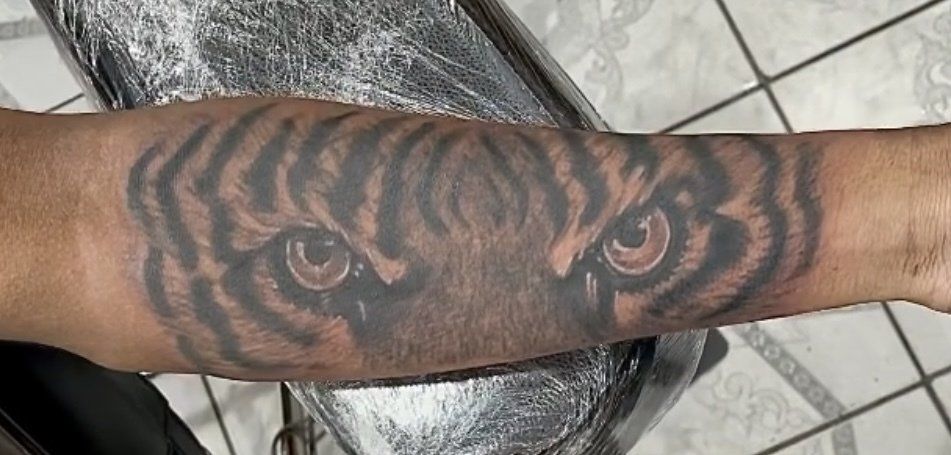 Tiger eye tattoo on a forearm, black stripes with detailed eye rendering.
