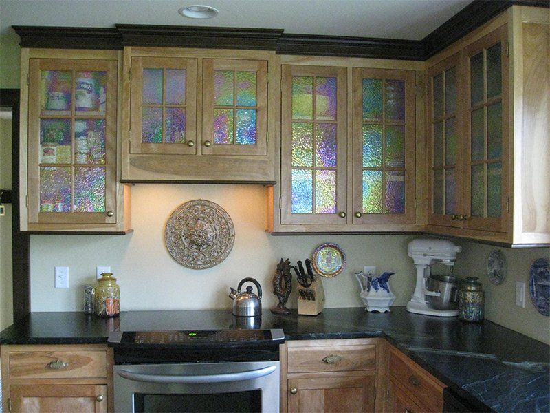 Kitchen with wooden cabinets, black countertops, and appliances beneath stained-glass cabinet doors.