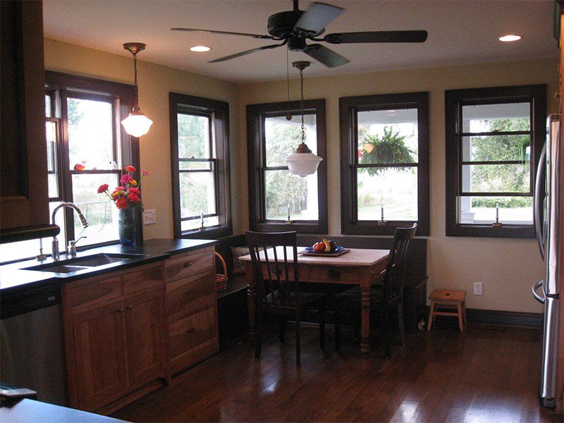 Modern kitchen with wood cabinets, island dining table, and large windows overlooking greenery