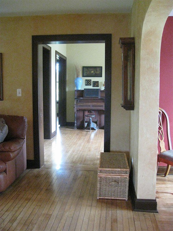 Hallway view into a sunlit room with wooden floors, a wicker basket, and a sofa on the left
