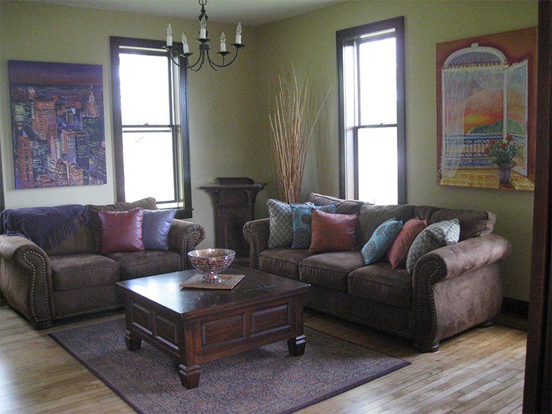 Living room with two sofas, a coffee table, framed art, and tall windows on green walls