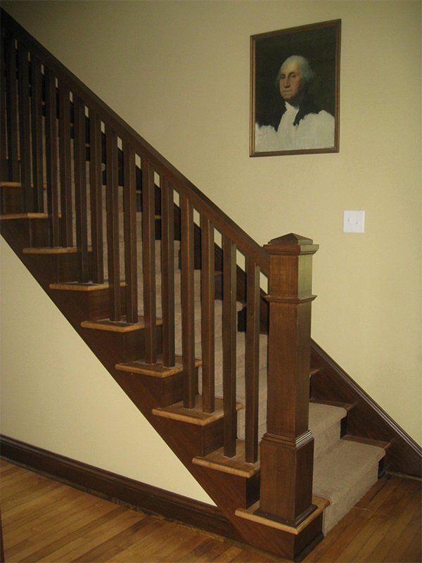 Wooden staircase with dark railings in a beige hallway, with a framed portrait on the wall.