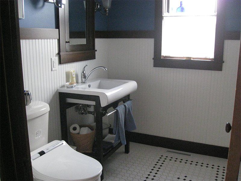 Small bathroom with toilet, sink, mirror, and tiled floor in black, white, and gray.