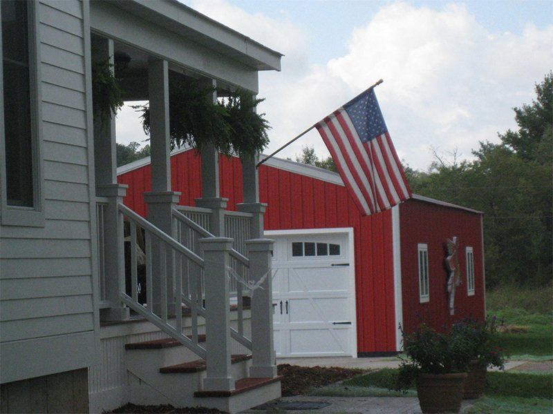 Front porch with hanging plants and an American flag beside a red garage on a cloudy day