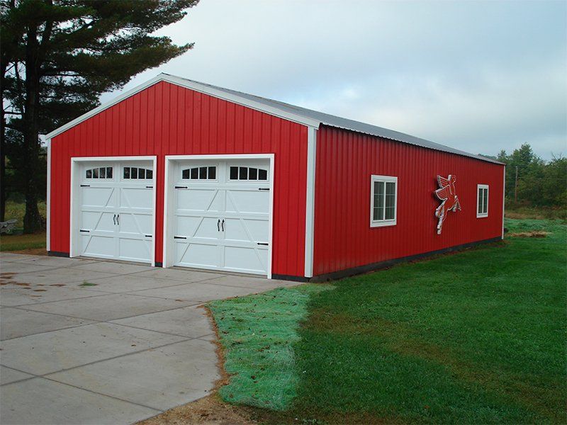 Red metal garage building with two white doors and windows beside a paved driveway and grass.