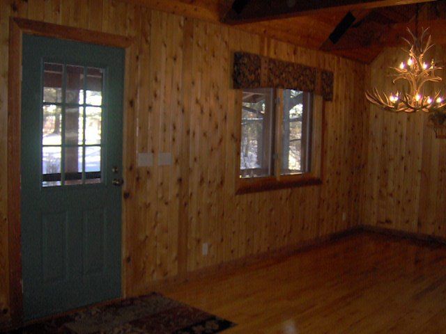 Wood-paneled room with a teal door, window, hardwood floor, and hanging chandelier.
