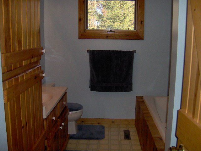 Small bathroom with wood cabinets, a window, towel rack, rug, and toilet visible.