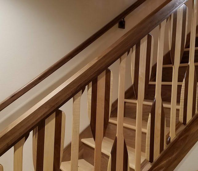 Wooden staircase railing with white balusters and a brown handrail along a stairwell wall